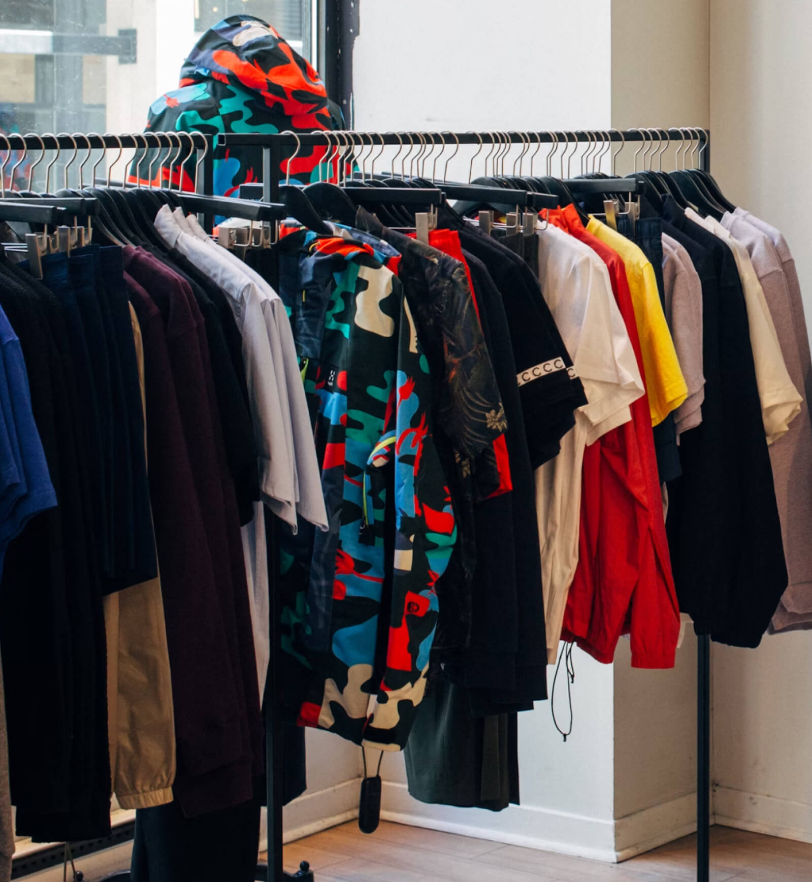 A rack of clothes in front of a window.